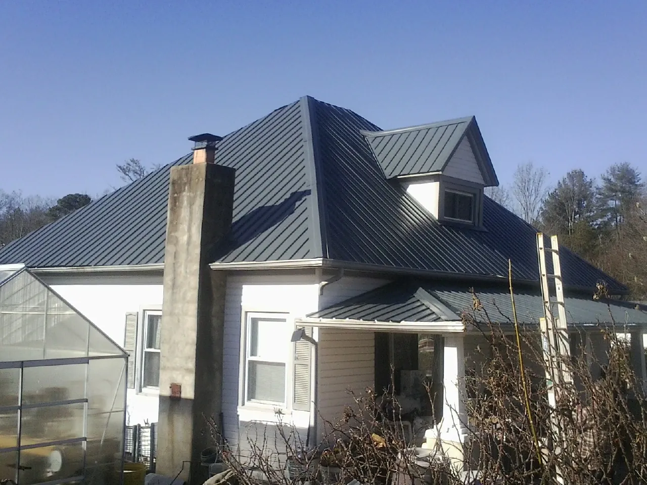 Dark blue standing seam metal roof on a white farmhouse with dormer — Slate & Tile Roof Repair by Roofing Brothers in Santa Fe